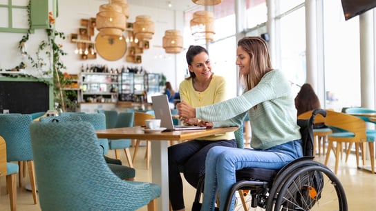 Young disabled woman having a good time with her friend in cafe. Тhey are spending time together, shopping online with credit card