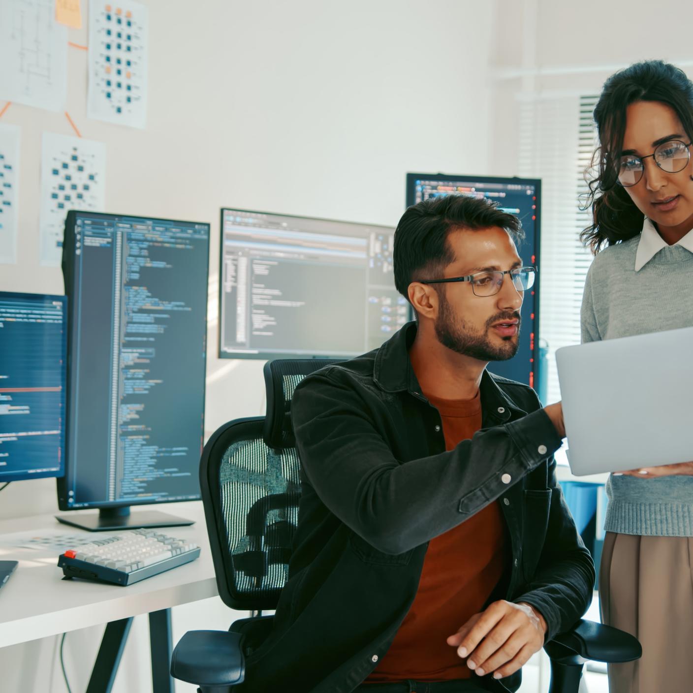 Two Hispanic programmers reviewing code on a laptop in a modern office