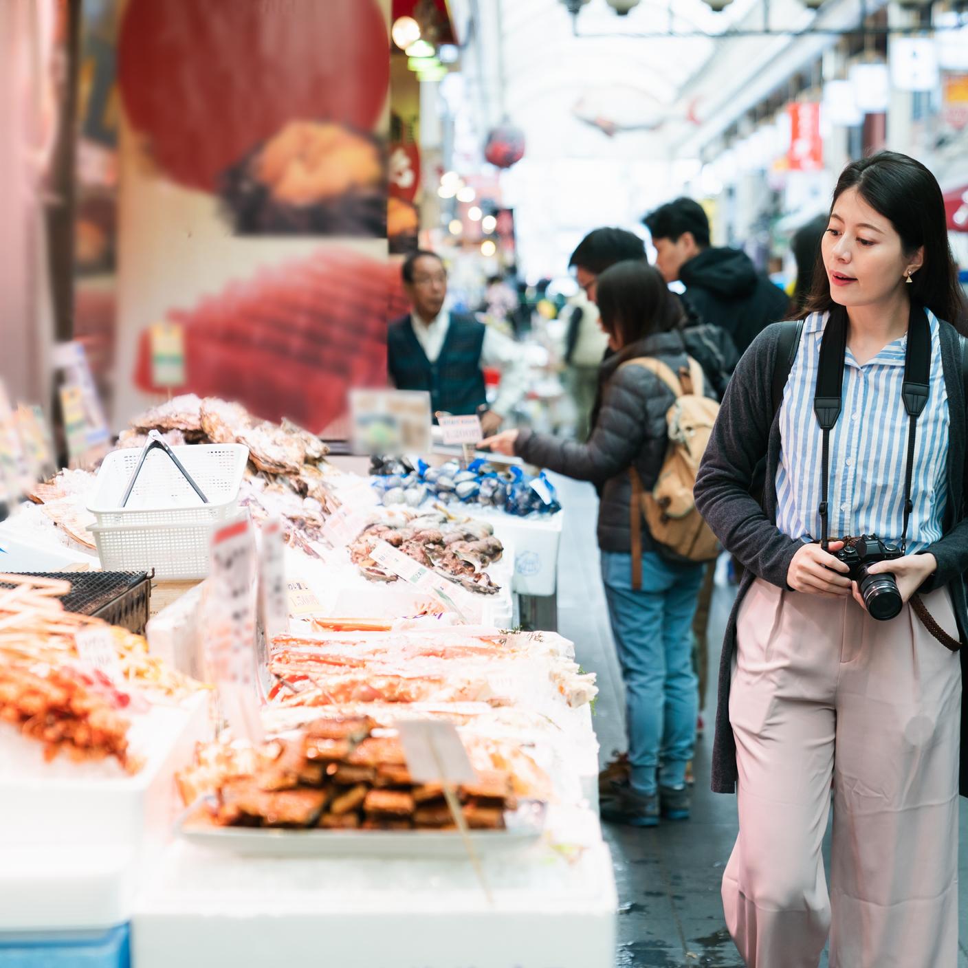 Building trust in temperature-sensitive supply chains - Asian woman traveler with camera passing by a local stall selling Japanese processed seafood