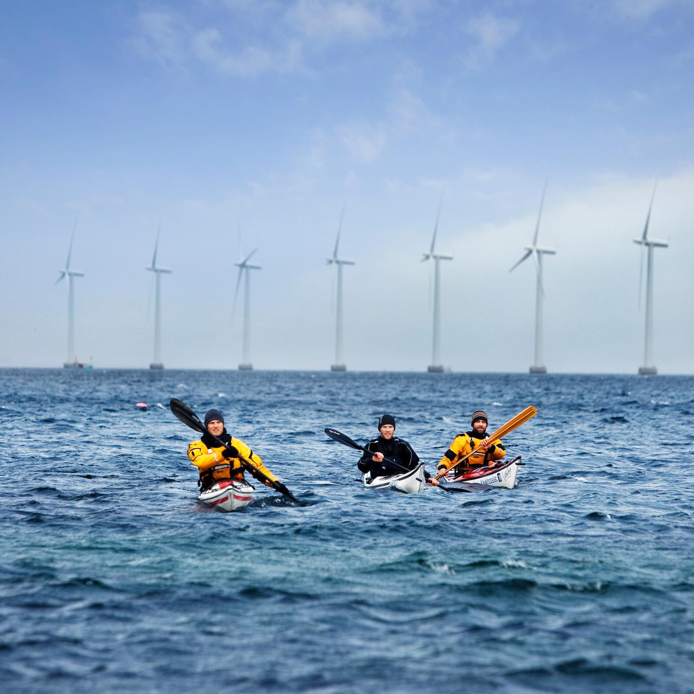 People in kayaks paddling towards wind turbines