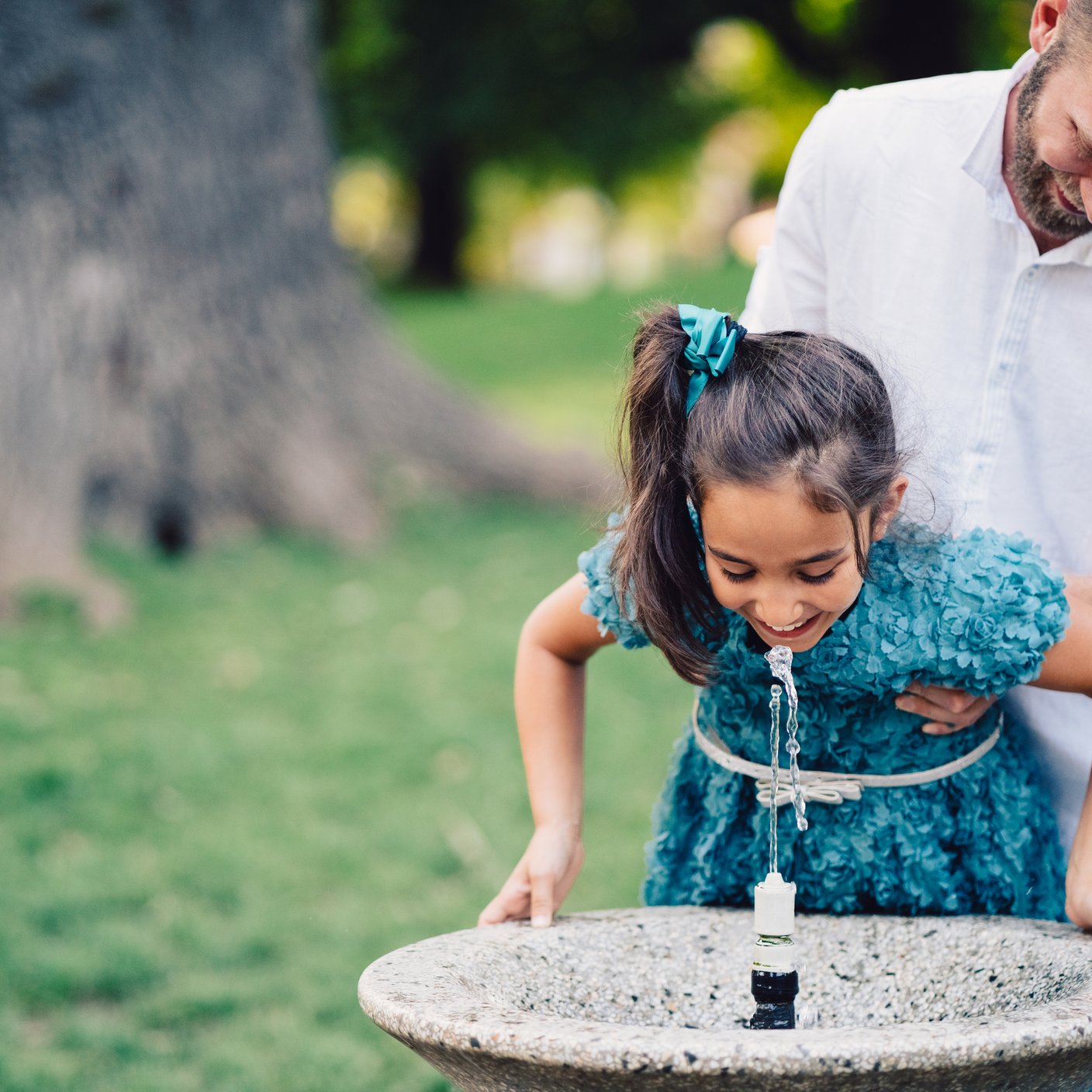 Young father and his daughter drinking water on hot summer day in the city park.