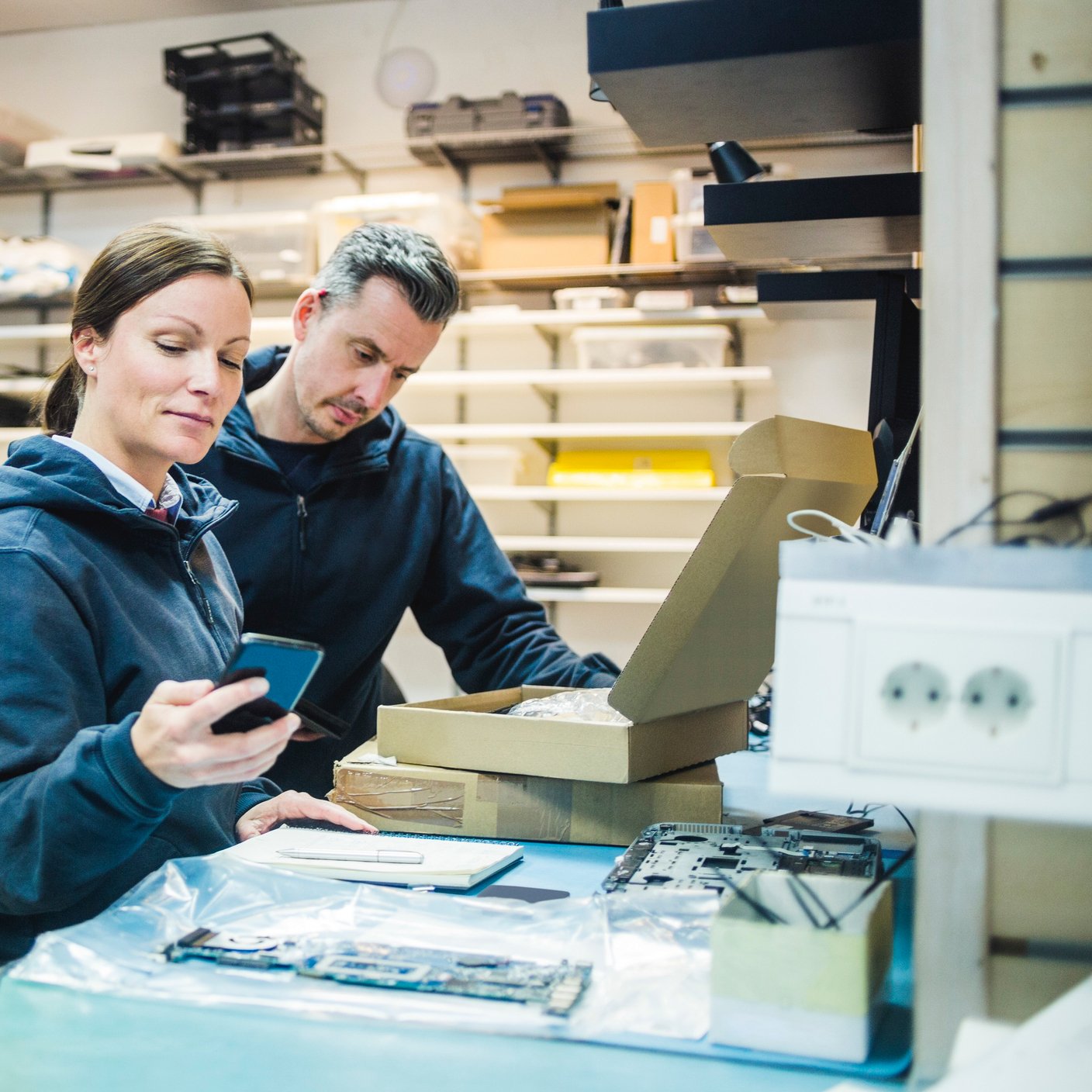 Mature female engineer using mobile phone by colleague in workshop.
