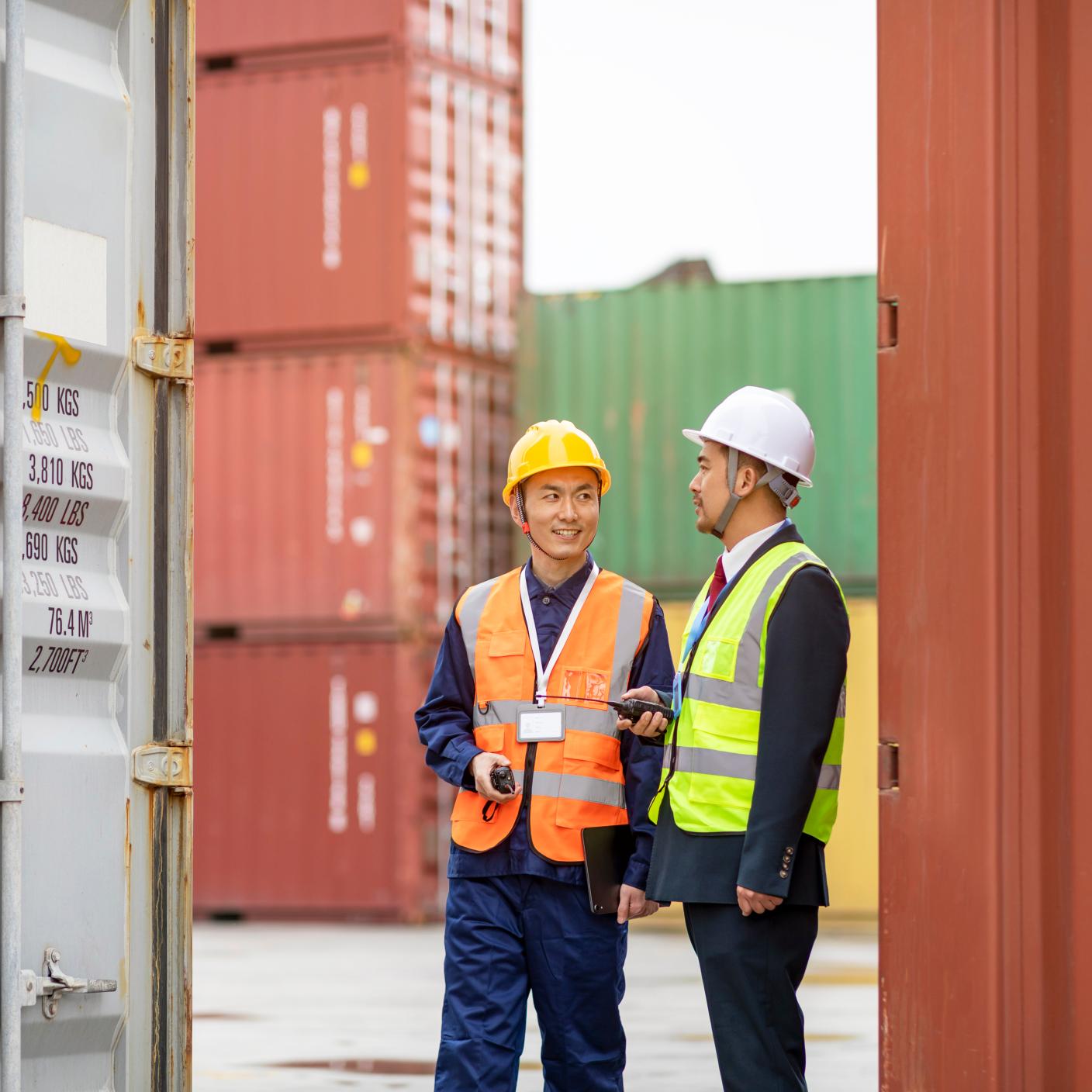 Male logistics operations manager discussion with male engineer to monitor overall cargo container operations on a shipping yard.Shipping Container Logistics and Storage Allocation in Field Operations.