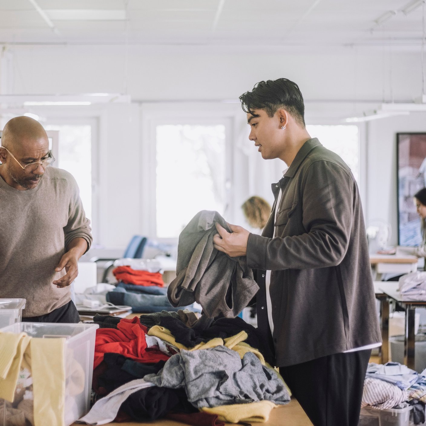 Fashion designers discussing with each other while sorting recycled clothes at workshop