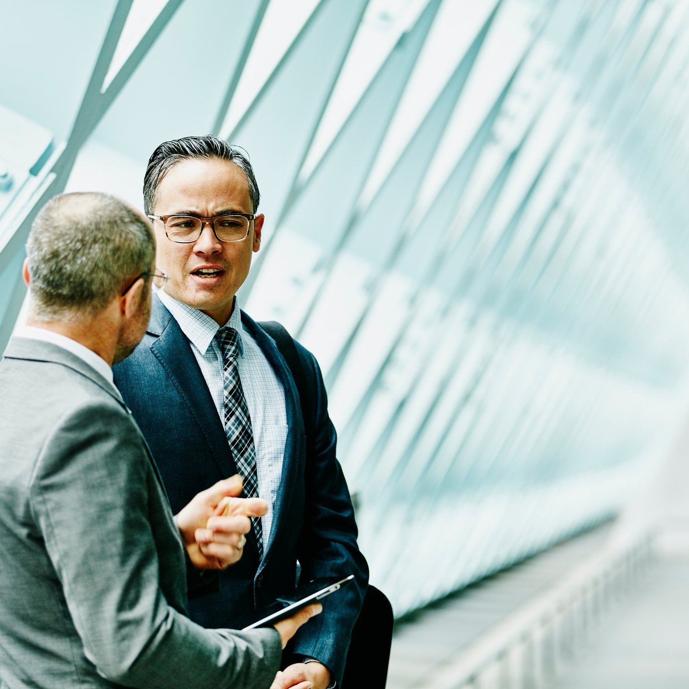 Deux hommes d’affaires discutent de données sur une tablette numérique lors d’une réunion informelle dans le couloir d’un bâtiment.