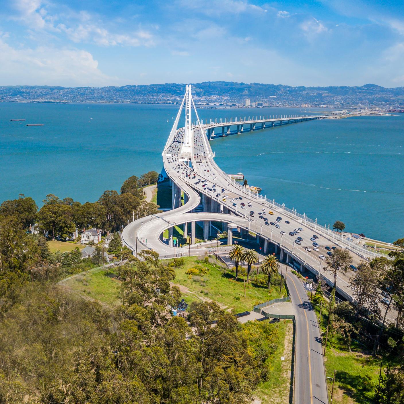 An aerial view of the Bay Bridge on a sunny day. A view from Treasure Island looking across the bay at Emeryville and Oakland. Ships and boats are in the Bay.