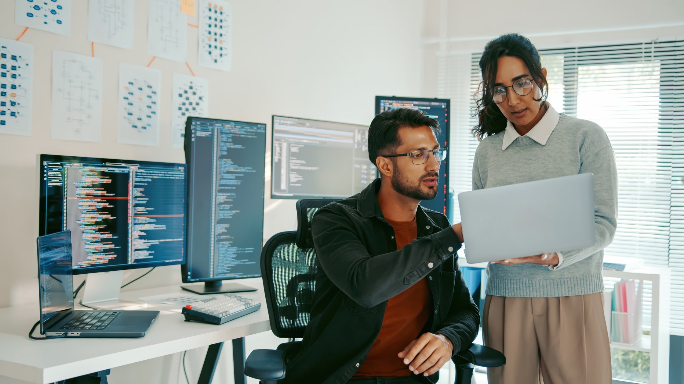Two programmers reviewing code on a laptop in a modern office.