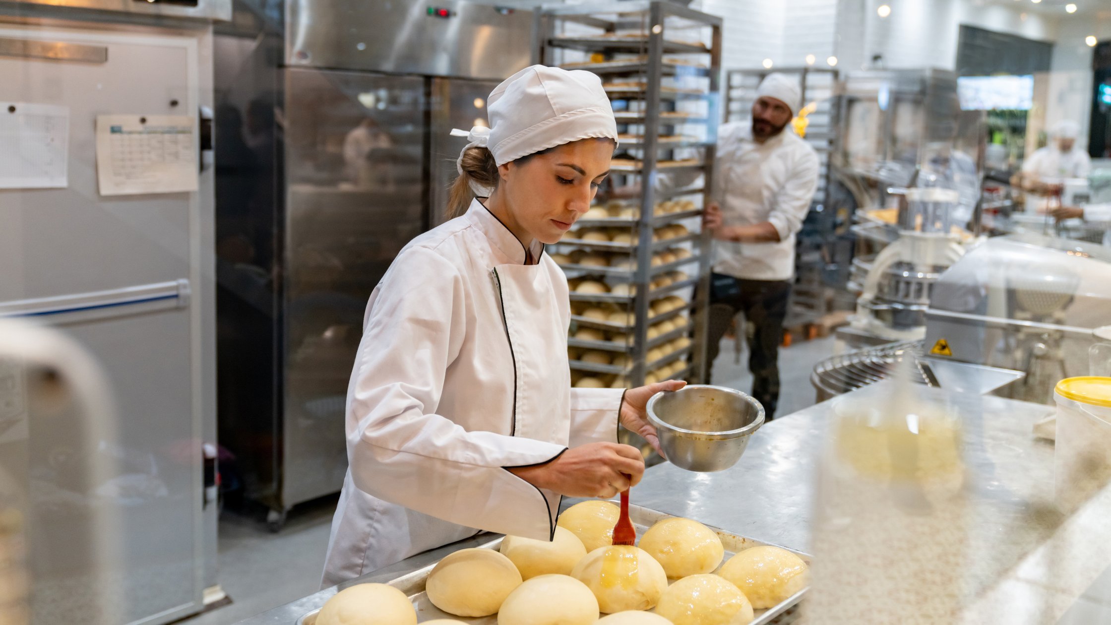Female baker spreading egg yolks on bread while baking at the bakery.