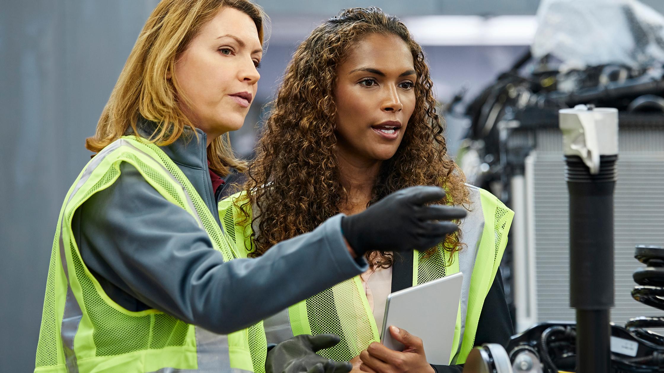 supervisor pointing to colleague by car part at factory