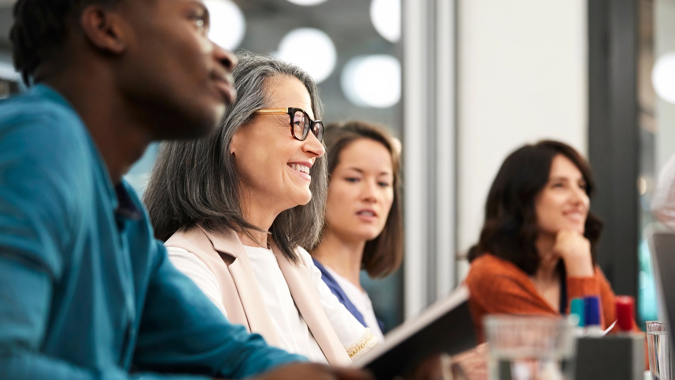 Smiling mature businesswoman sitting with colleagues while looking away. 