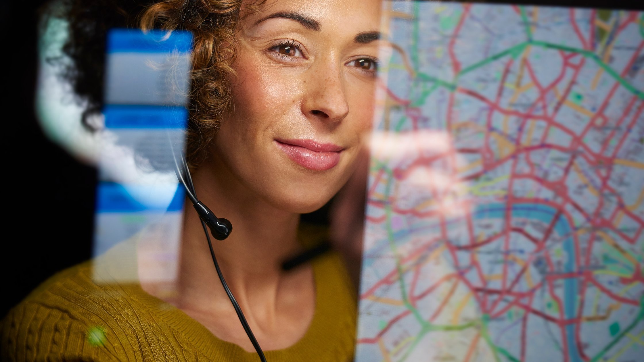A female logistics worker is organising dispatch of freight on her interactive digital map whilst talking on her headset.