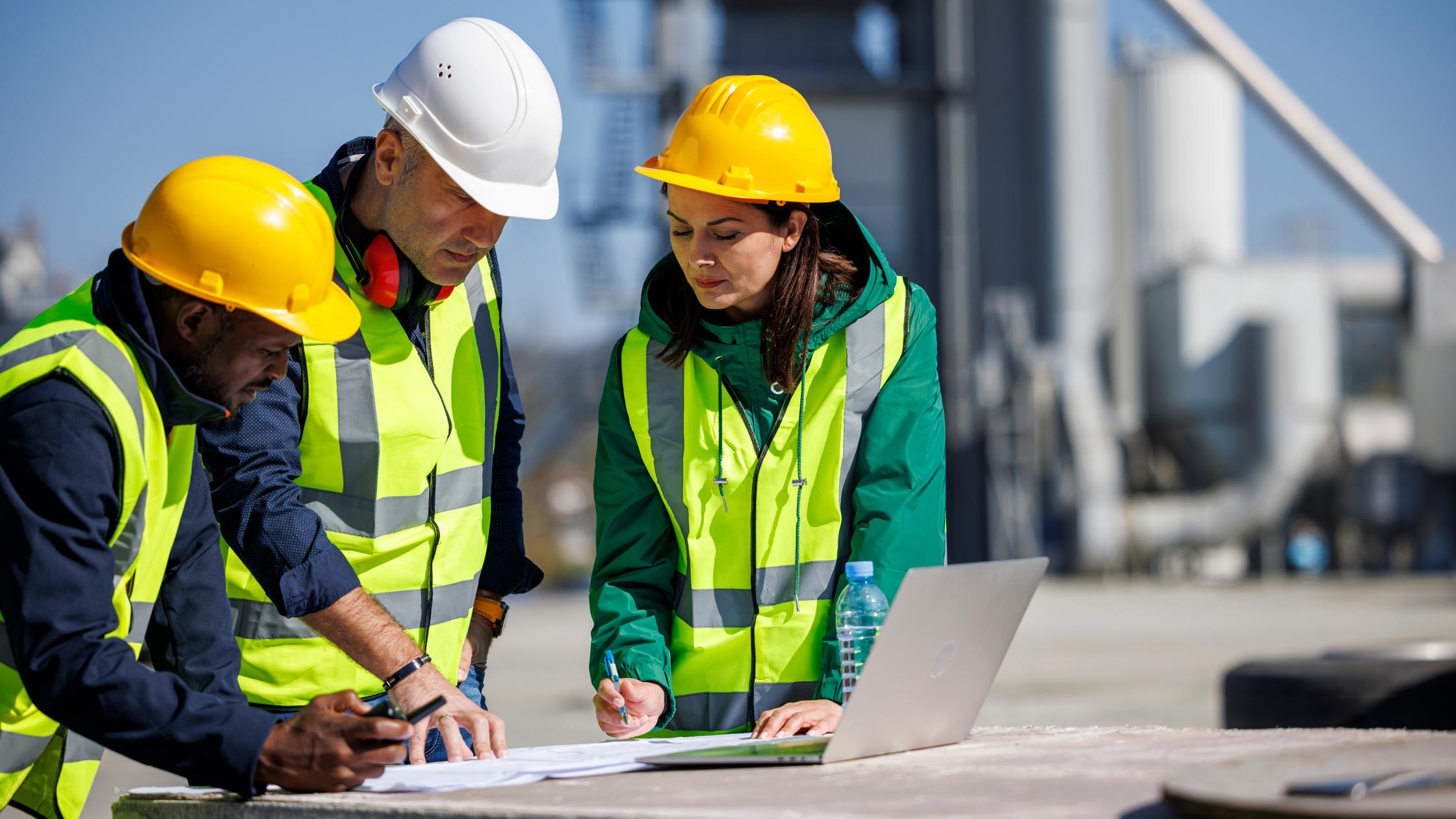 Three engineers in safety attire discussing at an industrial facility